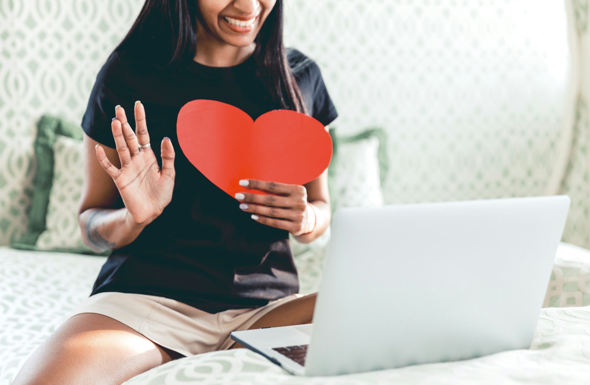 A woman happily chatting with lover, holding a heart, love during COVID, long distance relationship