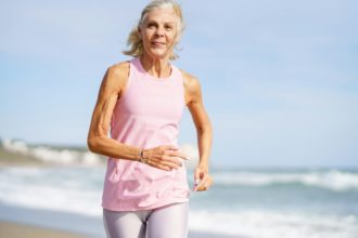 Older female doing sport to keep fit. Mature woman running along the shore of the beach